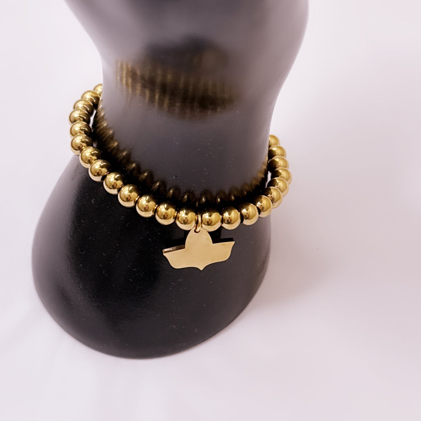 Side view of a gold-plated beaded stretch bracelet with official Alpha Kappa Alpha Ivy charm displayed on a black cylindrical stand.
