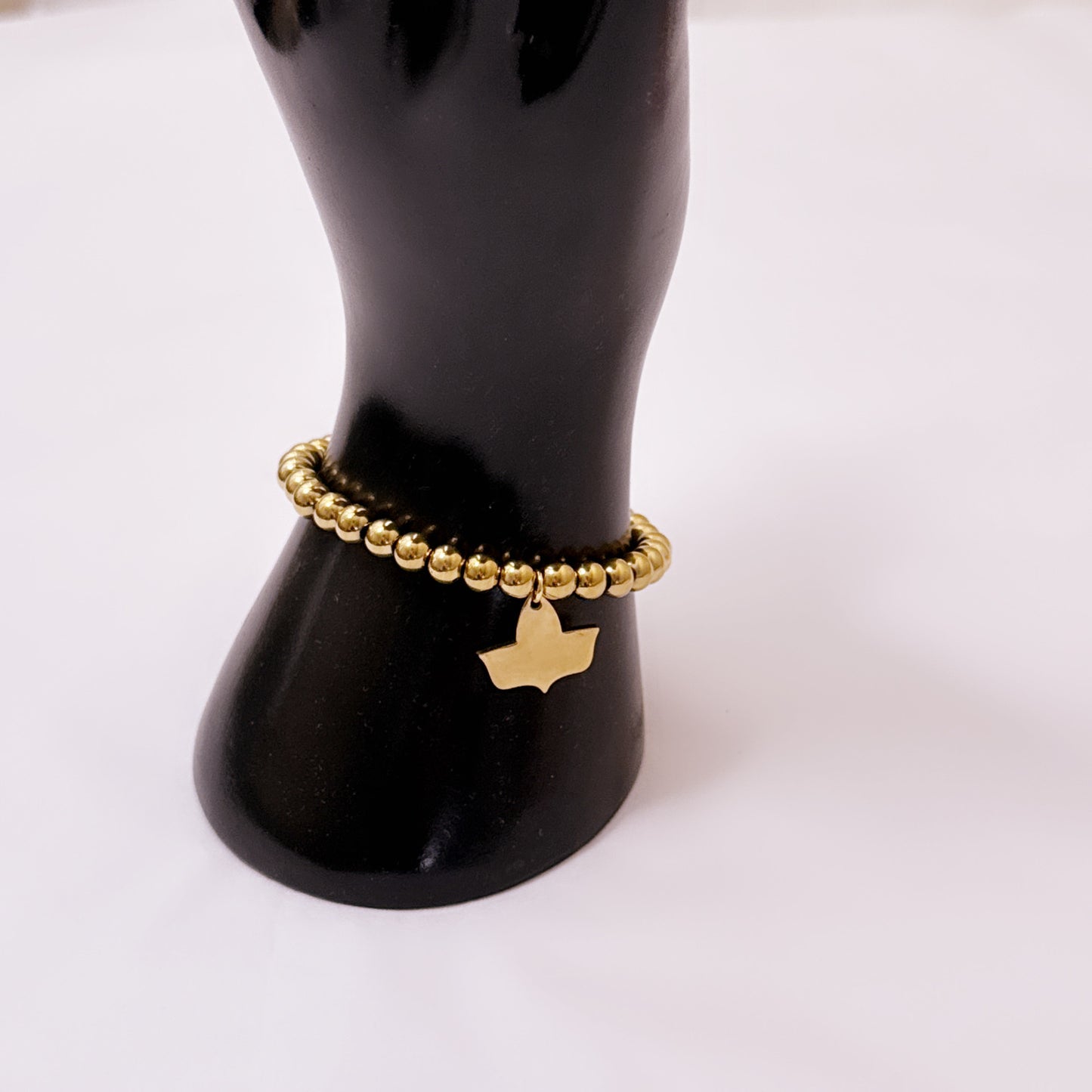 Gold-plated beaded stretch bracelet with official Alpha Kappa Alpha Ivy charm displayed on a black mannequin hand against a white background.