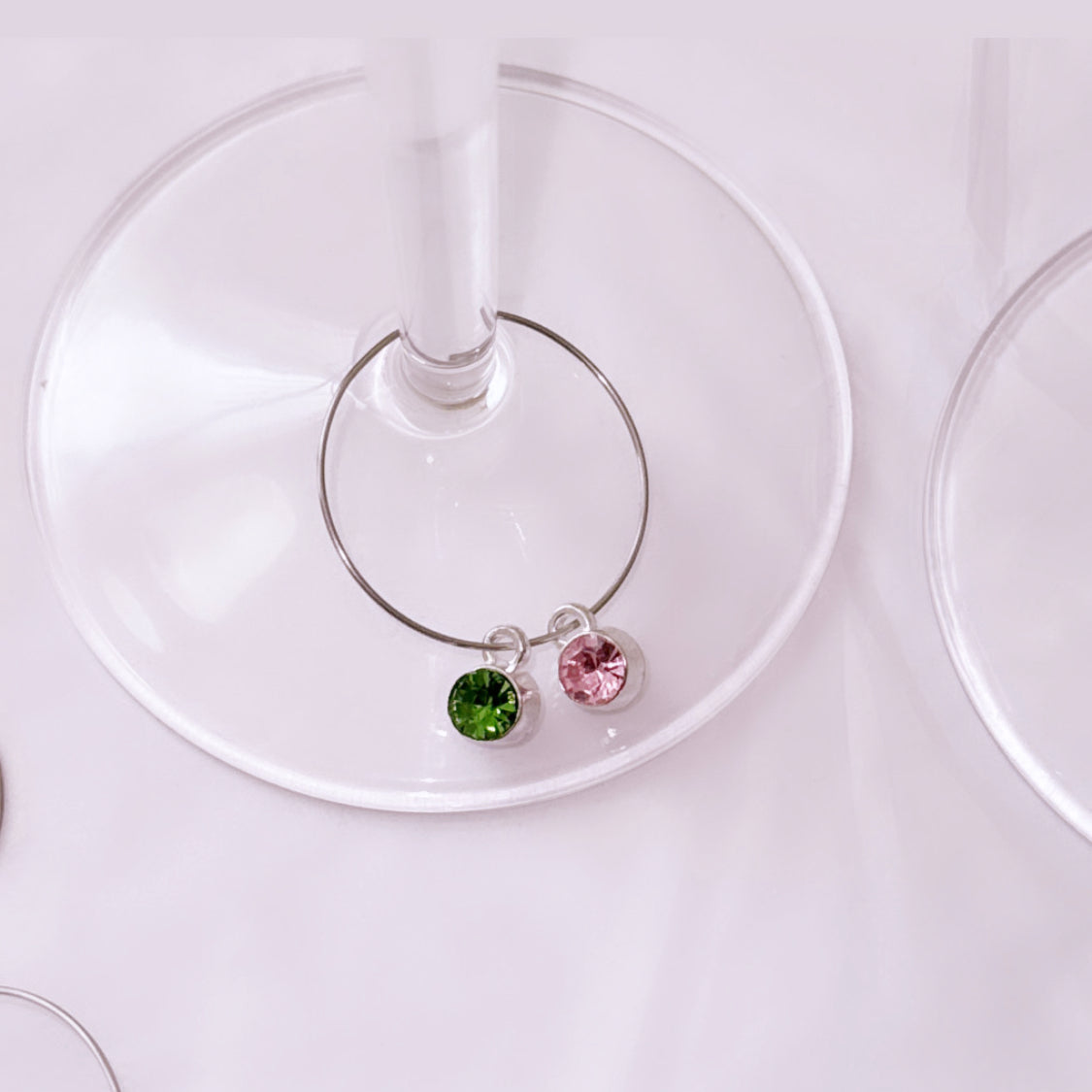 Wine glass charm with green and pink gemstones on a white background