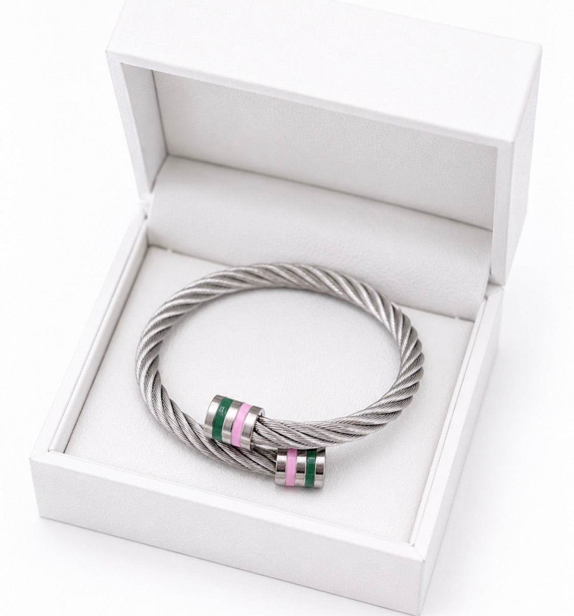 Adjustable stainless steel cable cuff bracelet with pink and green enamel accents, silver twisted wire design, presented in a white jewelry gift box.