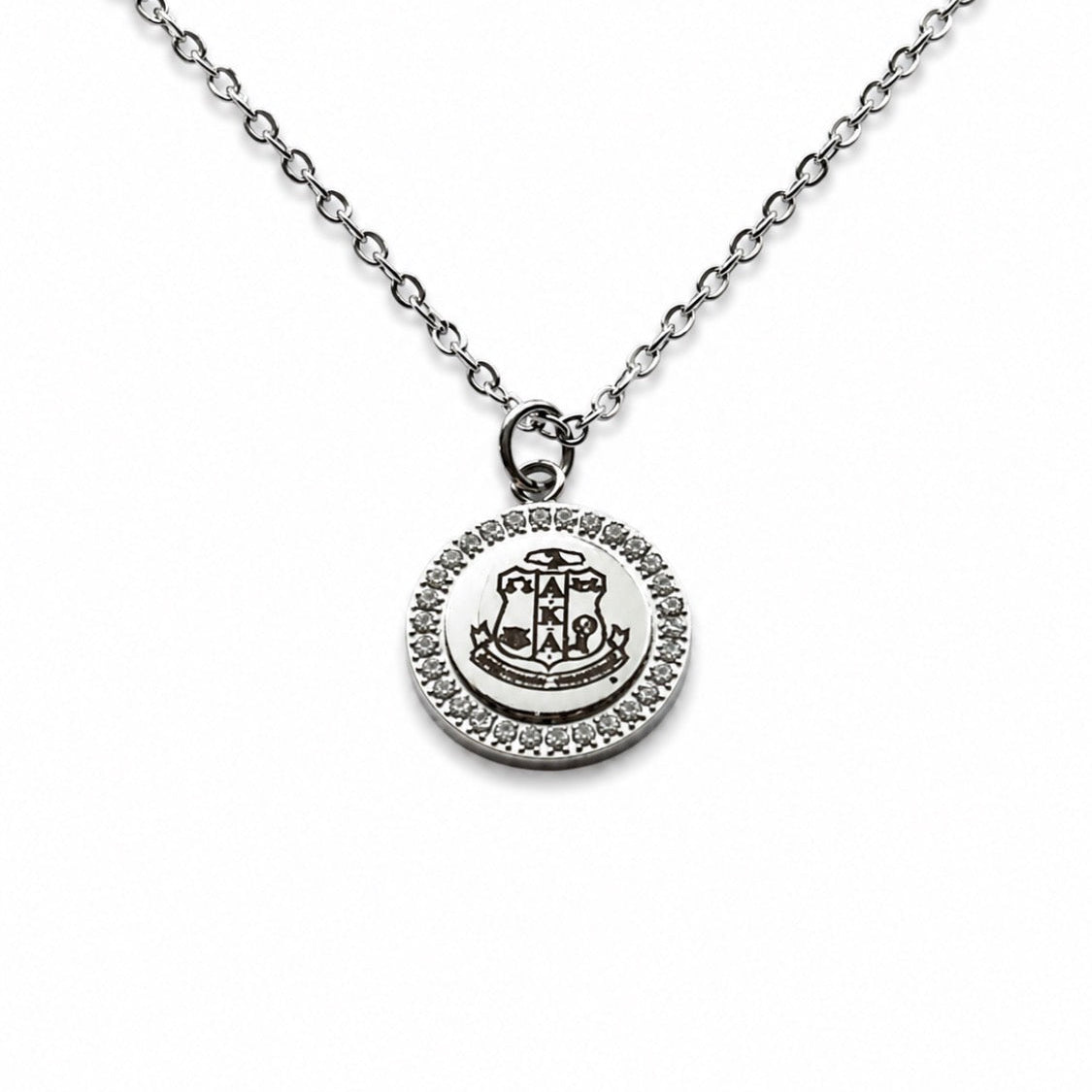 A silver-toned chain necklace with a round pendant featuring a central crest and a halo of small clear stones, shown on a plain white background.