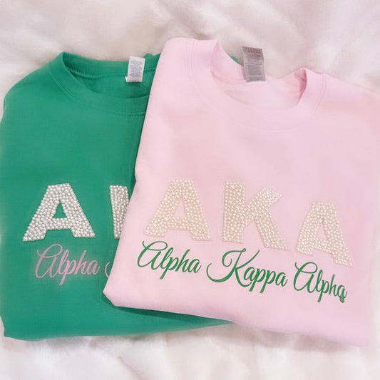 "Unisex AKA Pearl Embellished Sweatshirt in pink or green, featuring the iconic 'AKA' in pearls, representing the legacy of Alpha Kappa Alpha Sorority, Inc. A stylish and elegant way to show sorority pride."