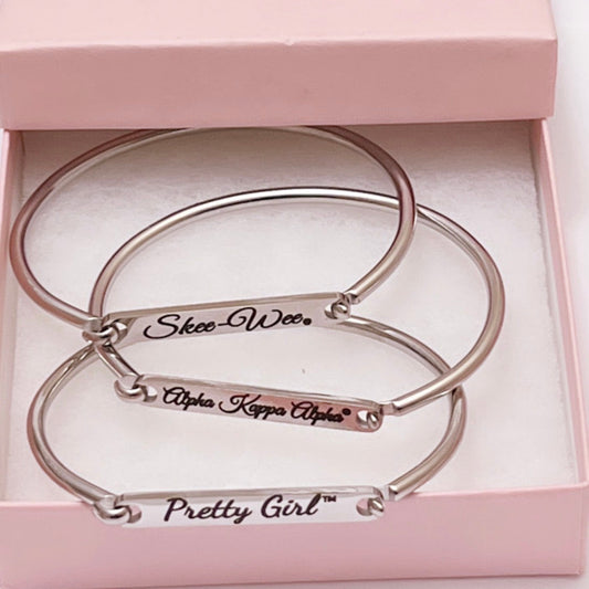 Three silver stainless steel bar cuff bracelets engraved with “Skee Wee,” “Alpha Kappa Alpha,” and “Pretty Girl,” displayed in a pink gift box.