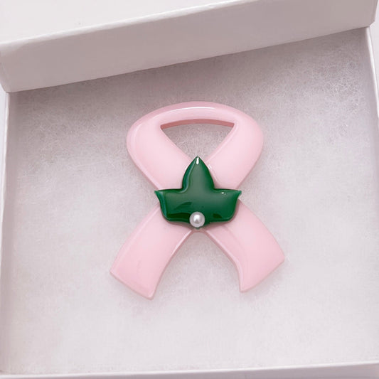 Pink ribbon brooch with green leaf and pearl center on a white gift box.