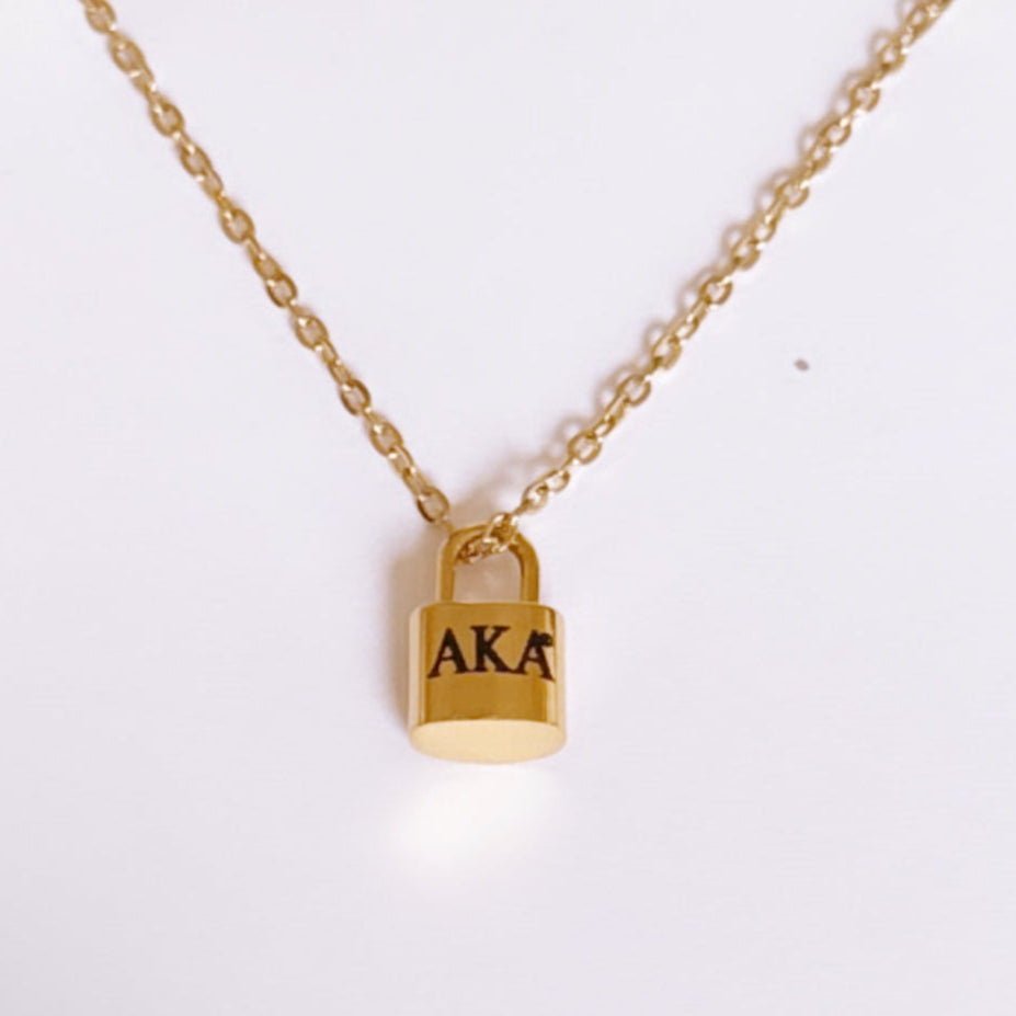 Gold padlock-shaped necklace with 'AKA' engraving on a white background