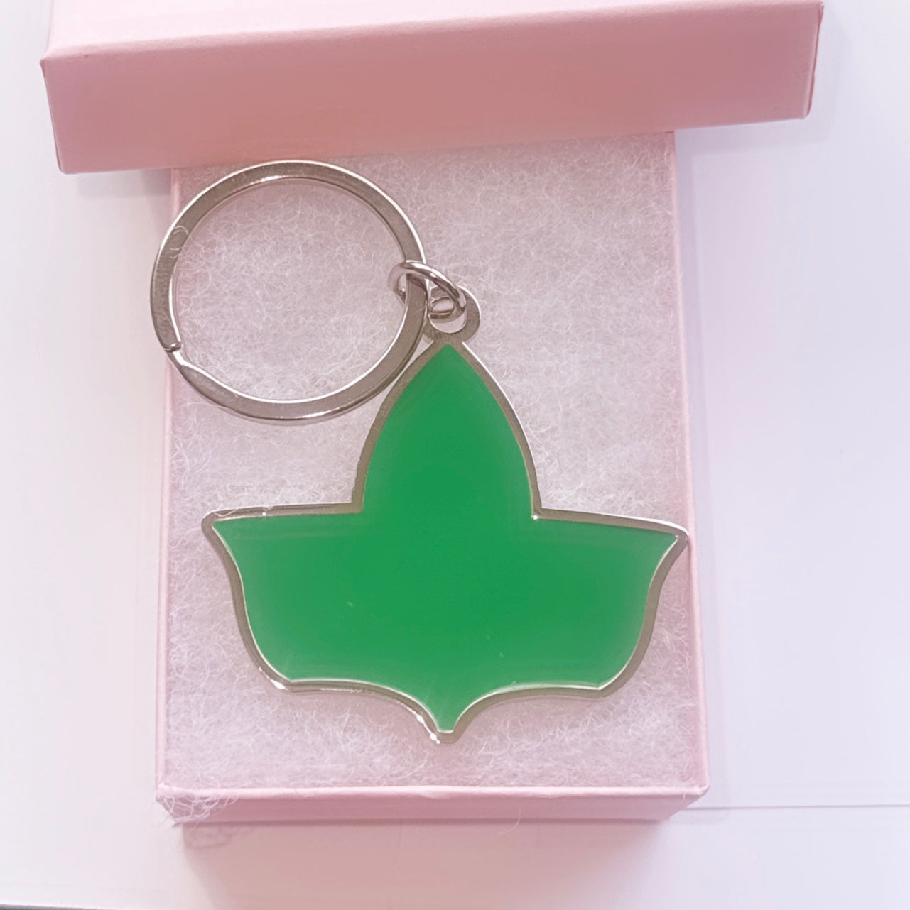 Green enamel side of the double-sided keychain featuring the official Ivy Leaf logo of Alpha Kappa Alpha Sorority, Inc., displayed in a pink gift box.