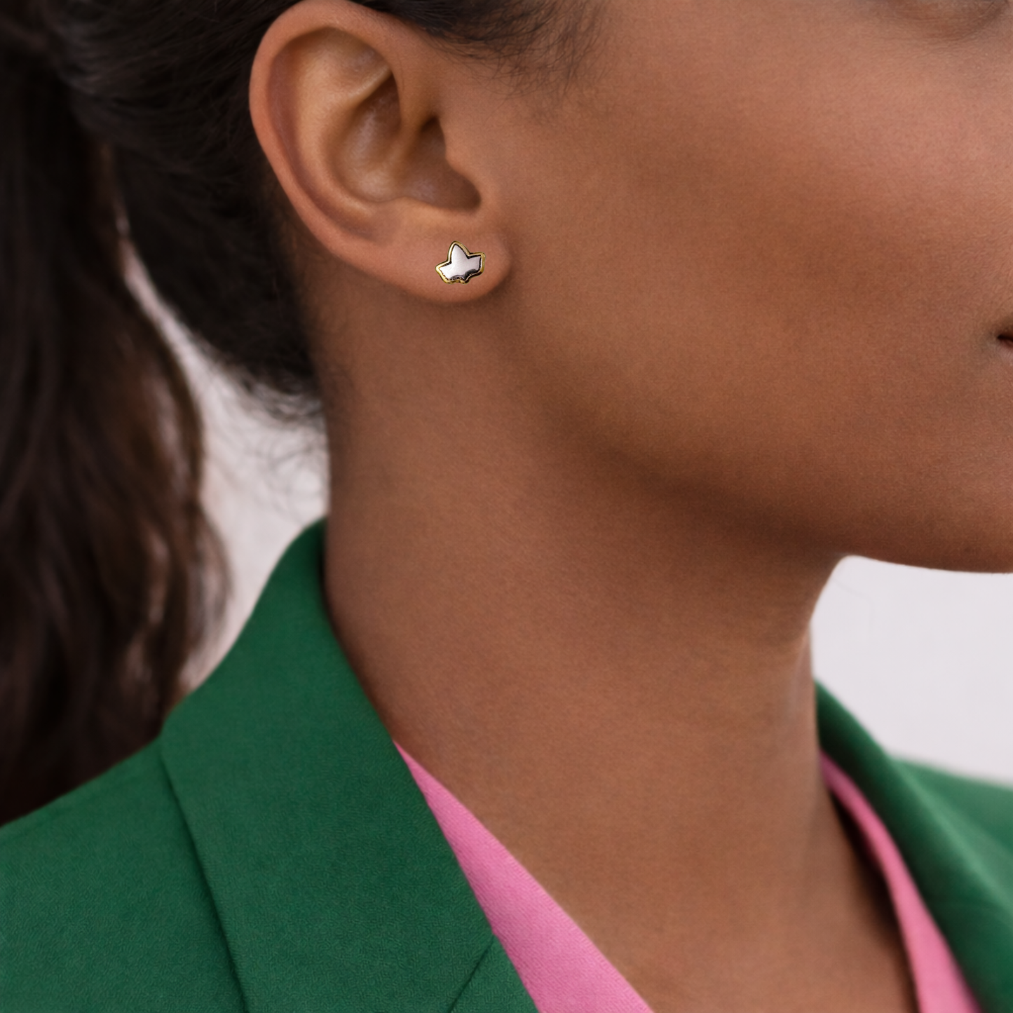 Close-up of an ear wearing a small earring with a green blazer and pink shirt in the background