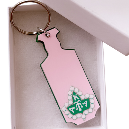 Pink keychain shaped like a dress with a green logo in a white box