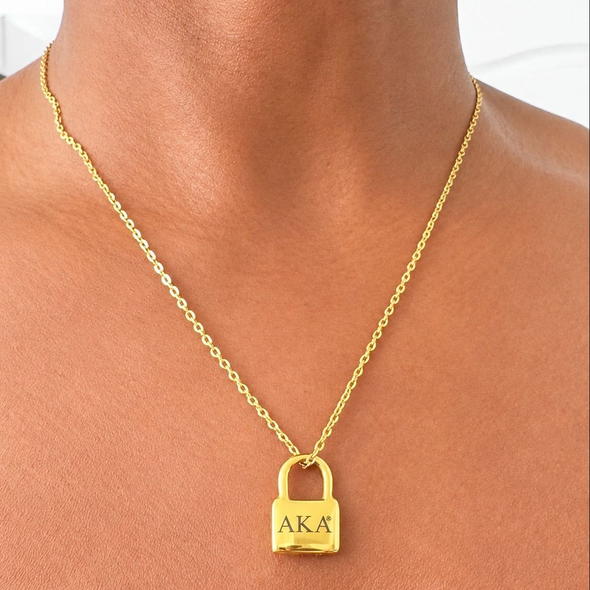 Gold tone AKA padlock pendant necklace worn by a model, showing the polished pendant and link chain.