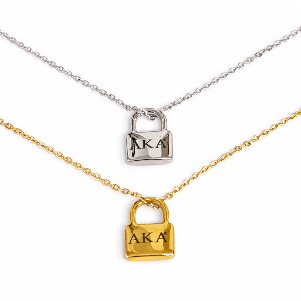 Two delicate necklace chains on a white background, one silver and one gold, each featuring a small padlock pendant engraved with the Greek letters 'AKA'.
