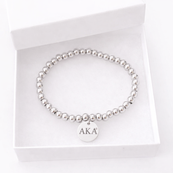 Alpha Kappa Alpha licensed silver beaded stretch bracelet with engraved AKA charm photographed in a pure white gift box
