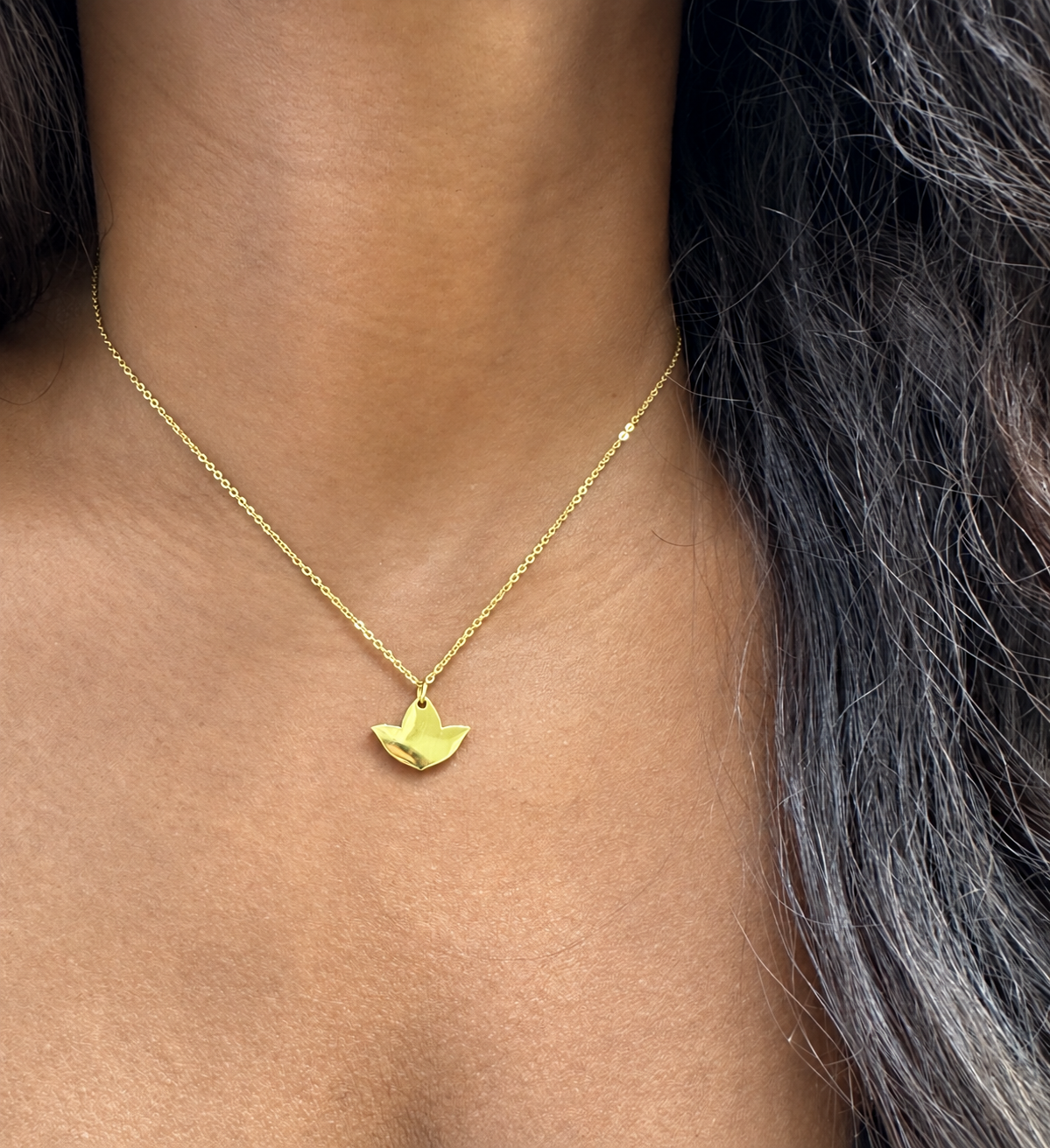 Model wearing a dainty gold ivy leaf pendant necklace resting below the collarbone.