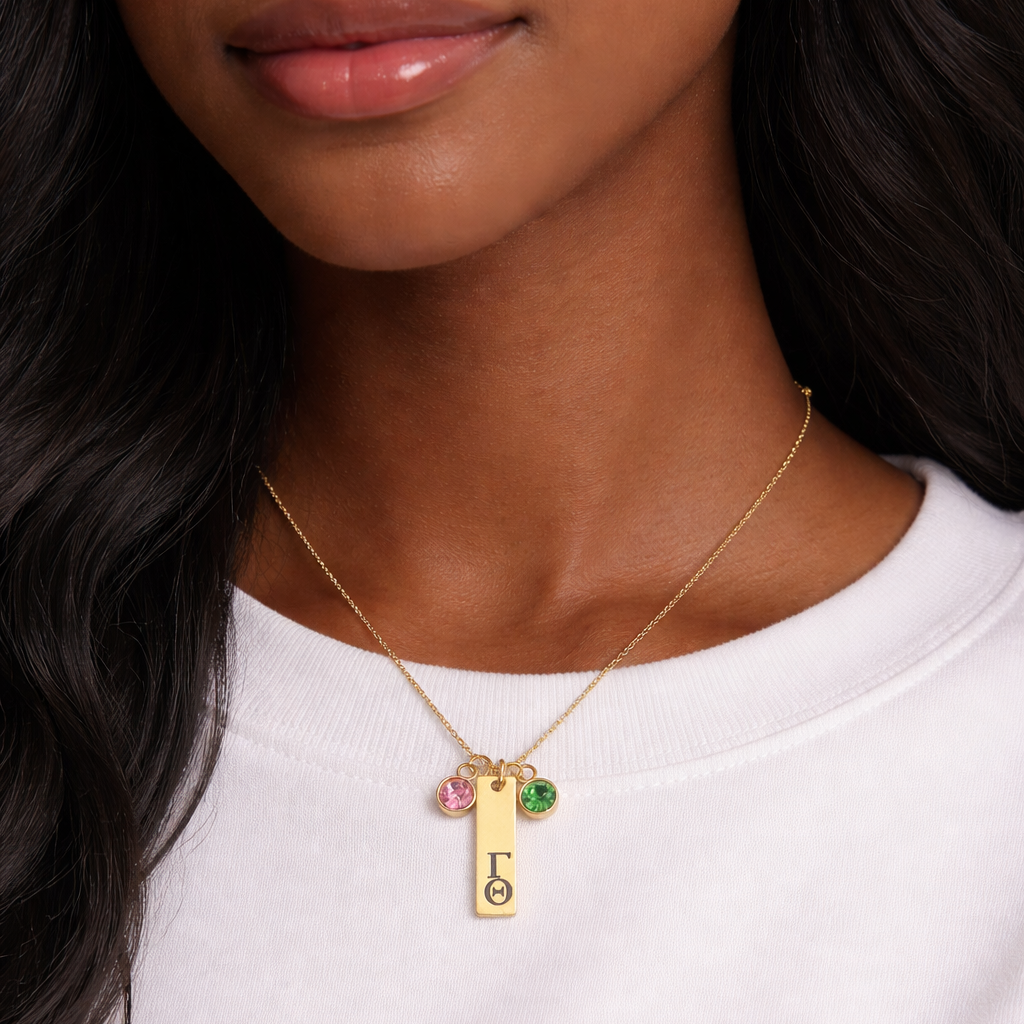 Gold personalized Greek letter charm necklace worn on model showcasing size and fit with pink and green crystal accents
