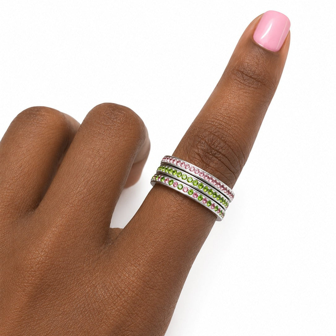 Model wearing three stainless steel stacking rings with pink, green, and alternating pink and green cubic zirconia stones on finger against a white background.