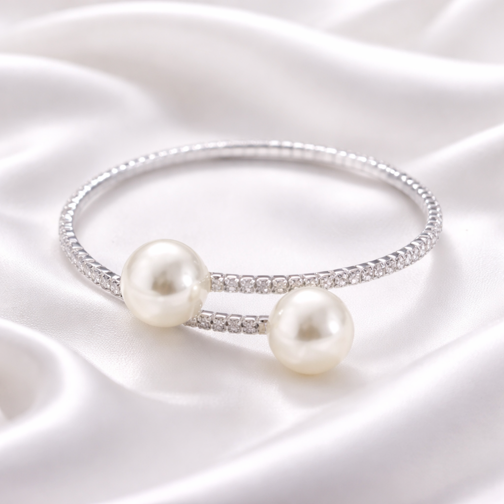 Silver open cuff pearl bracelet with crystal detailing displayed on white silk fabric