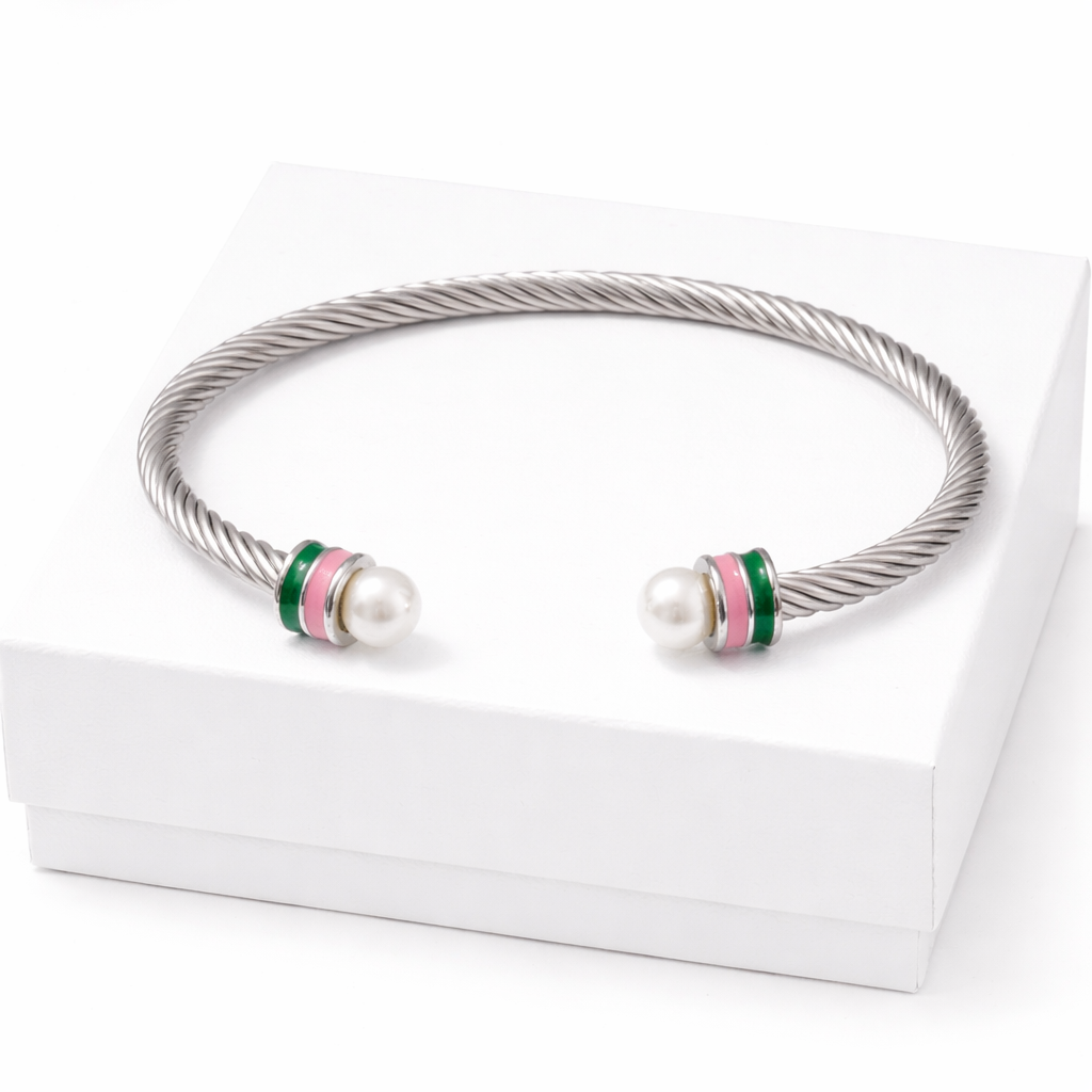 Stainless steel cable cuff bracelet with pearl ends and pink and green enamel accents displayed on a white gift box