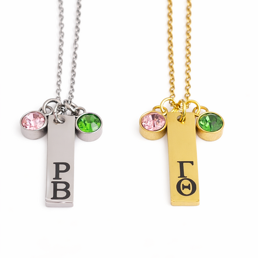 Personalized stainless steel charm necklaces in gold and silver with engraved Greek letters and pink and green charms accents on white background
