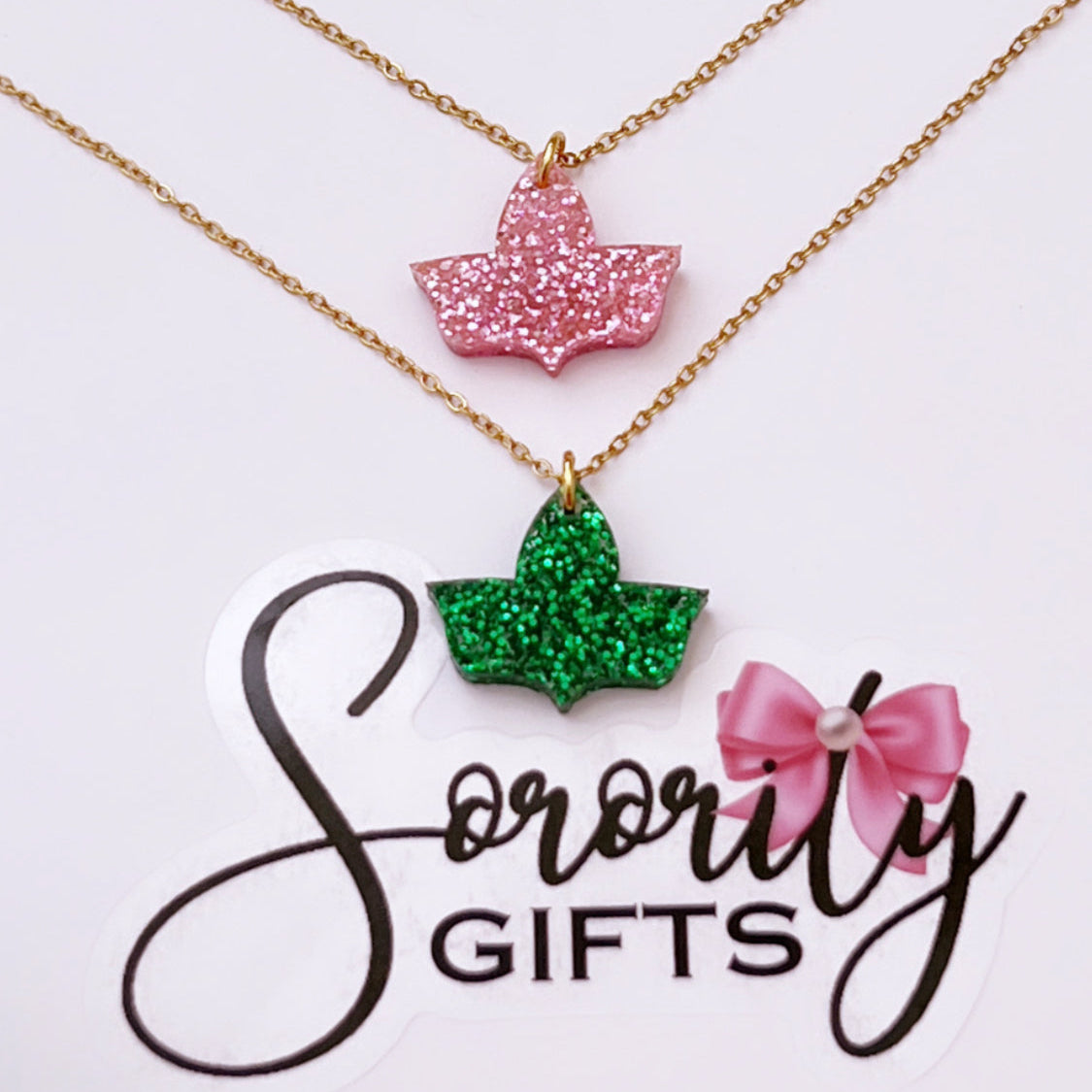 Two ivy leaf pendant necklaces with gold chains are displayed—one in pink glitter and the other in green glitter—on a white backing card with the "Sorority Gifts" logo featuring a pink bow.