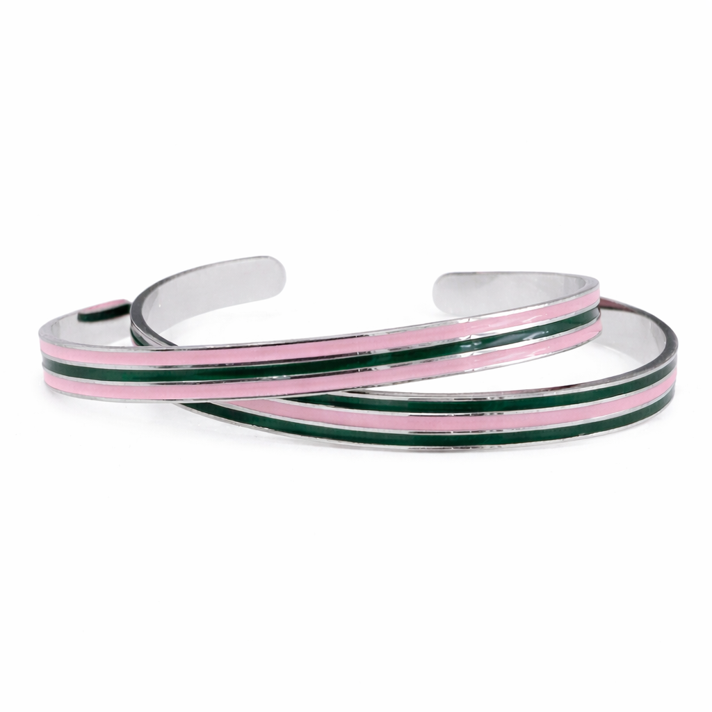 Two slim stainless steel cuff bracelets with pink and green enamel stripes displayed on a pure white background