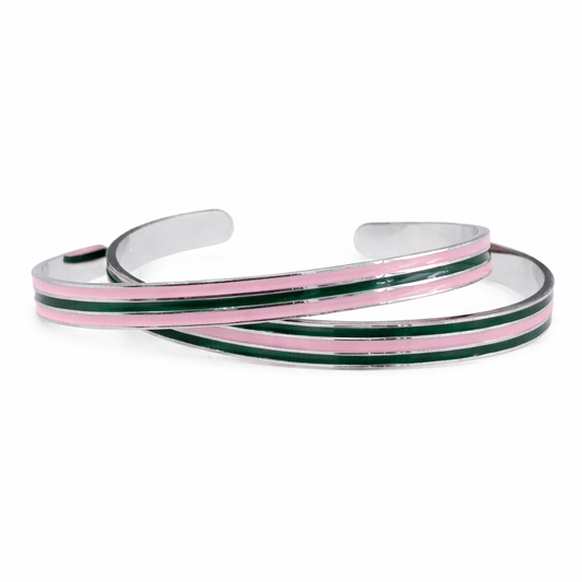 Two slim stainless steel cuff bracelets with pink and green enamel stripes displayed on a pure white background