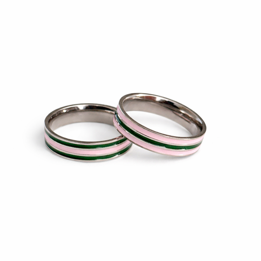 Two stainless steel rings with pink and green striped enamel bands displayed together on a white background.