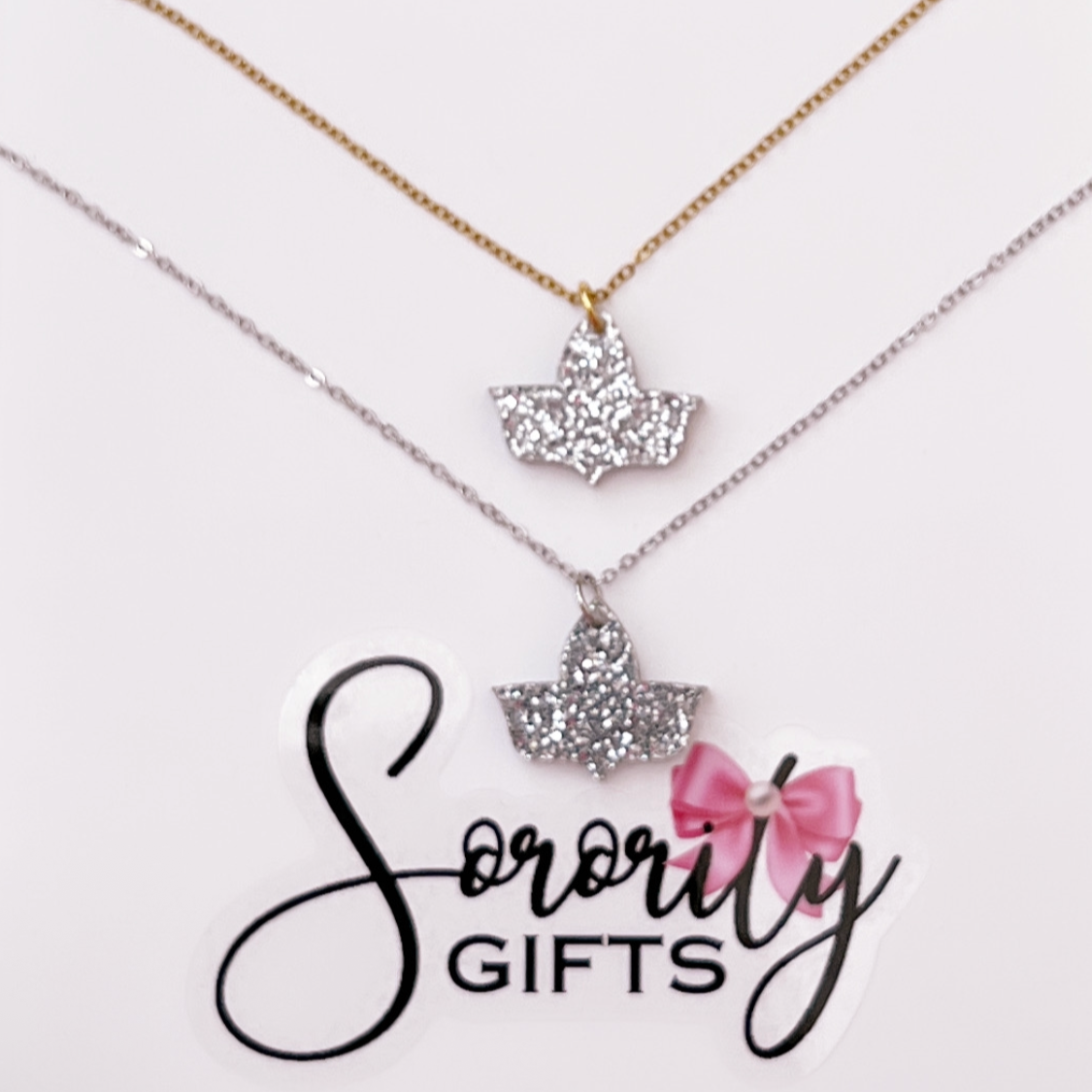 Two silver glitter ivy leaf pendant necklaces displayed on a white backing card with the "Sorority Gifts" logo. One necklace features a gold chain, and the other has a silver chain.