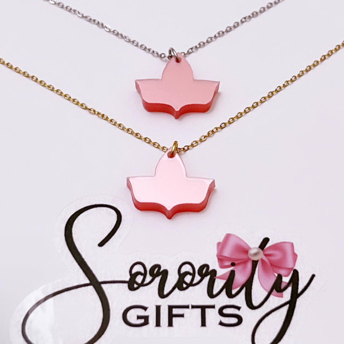 Two solid pink ivy leaf pendant necklaces displayed on a white card with the "Sorority Gifts" logo. One necklace features a silver chain and the other has a gold chain.